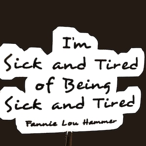 May include: A white sign with black text that reads "I'm sick and tired of being sick and tired" with the name "Fannie Lou Hammer" at the bottom.