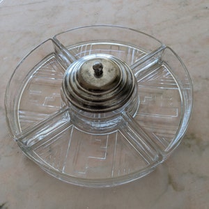 Puede incluir: Un plato de servir de vidrio transparente con una tapa de plata. El plato tiene cinco secciones y está decorado con un patrón geométrico.