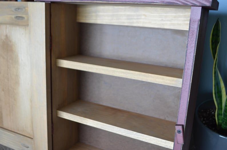 Puede incluir: Un armario de madera con una sola puerta y tres estantes. El armario est&aacute; pintado de un color marr&oacute;n claro con un ribete marr&oacute;n m&aacute;s oscuro. La puerta est&aacute; cerrada y los estantes est&aacute;n vac&iacute;os.