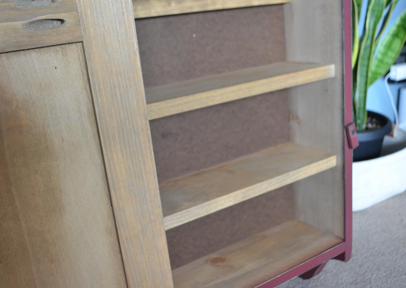 Puede incluir: Un armario de madera con marco rojo y tres estantes. El armario tiene una sola puerta en el lado izquierdo.