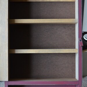 Puede incluir: Una peque&ntilde;a estanter&iacute;a de pared de madera con un acabado rojo burdeos. La estanter&iacute;a tiene tres estantes y dos ganchos en la parte inferior. La estanter&iacute;a est&aacute; vac&iacute;a.