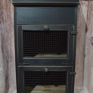 May include: Black wooden storage cabinet with two wire mesh doors and a hinged top lid. The cabinet has a distressed finish and black metal hinges.