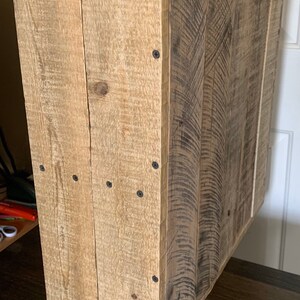 May include: A rustic wooden cabinet made from reclaimed wood. The cabinet has a natural wood colour and features a single door and a shelf. It is ideal for storing small items or displaying decorative objects.
