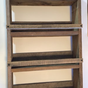 May include: A rustic wooden shelf unit with four shelves. The shelves are made of reclaimed wood and have a natural, weathered finish. The shelf unit is mounted to a wall and is perfect for displaying small items or organizing a space.