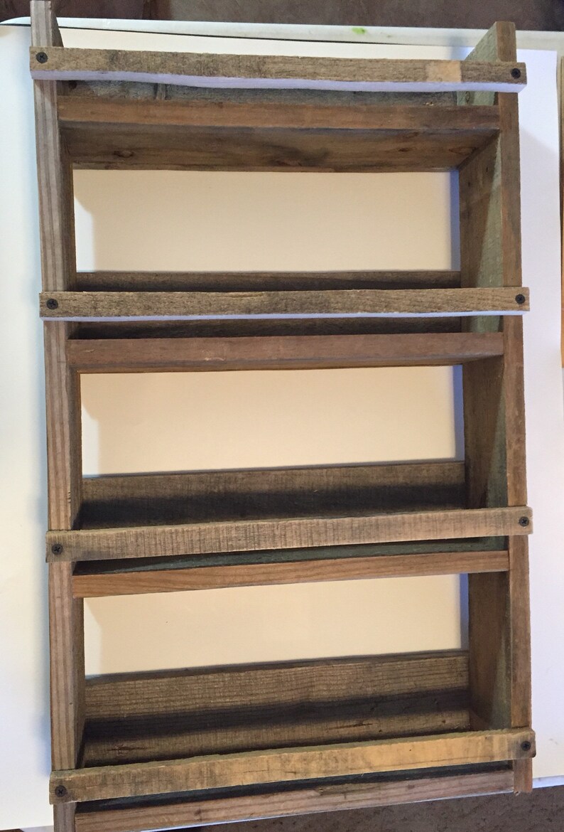 May include: A rustic wooden shelf unit with four shelves. The shelves are made of reclaimed wood and have a natural, weathered finish. The shelf unit is mounted to a wall and is perfect for displaying small items or organizing a space.