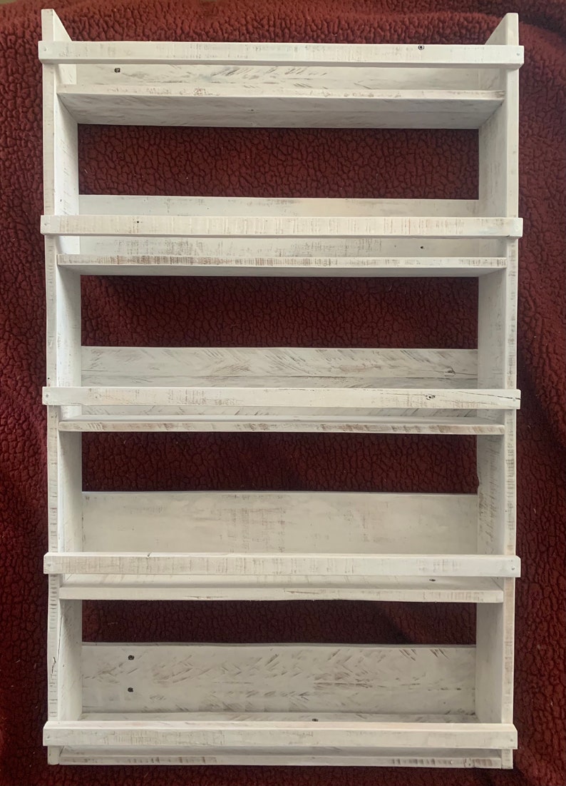 May include: White wooden wall mounted shelf unit with five shelves. The shelves have a distressed white finish and are perfect for displaying small items.