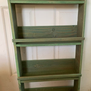 May include: A green wooden shelf unit with four shelves. The shelves are made of rustic wood and have a distressed finish.