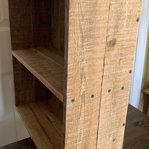 May include: A rustic wooden shelf unit with two shelves. The shelf is made of reclaimed wood and has a natural finish. The shelf is held together with screws.