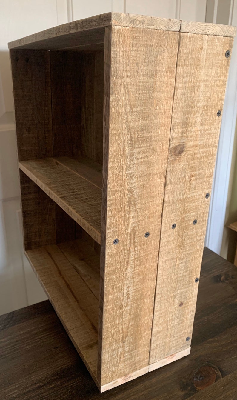 May include: A rustic wooden shelf unit with two shelves. The shelf is made of reclaimed wood and has a natural finish. The shelf is held together with screws.