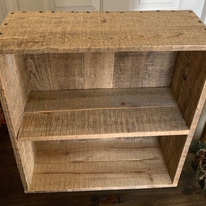 May include: A rustic wooden shelf unit with two shelves. The shelf is made of reclaimed wood and has a natural finish. The shelf is ideal for displaying books, plants, or other decorative items.