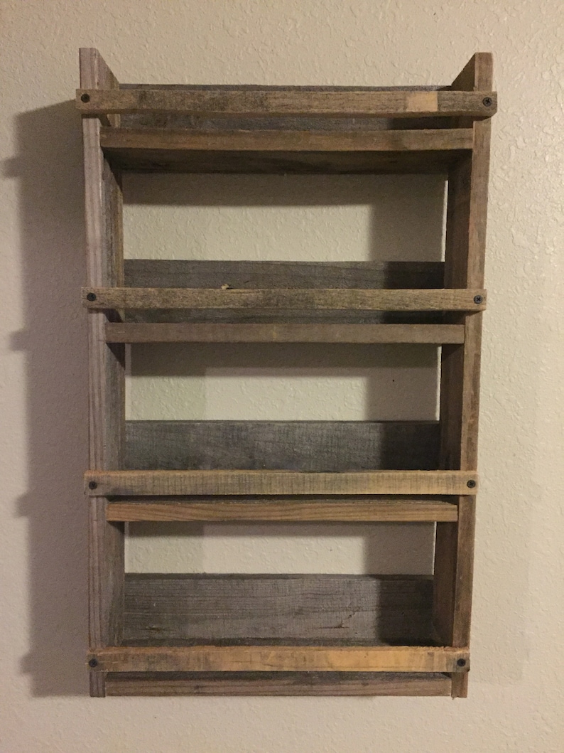 May include: A rustic wooden shelf unit with four shelves. The shelves are made of reclaimed wood and have a natural, weathered finish. The shelf unit is mounted to a wall and has a simple, farmhouse style.