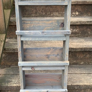 May include: A gray wooden shelf unit with four shelves. The shelves are made of reclaimed wood and have a rustic look. The shelf unit is perfect for displaying small items or organizing a small space.