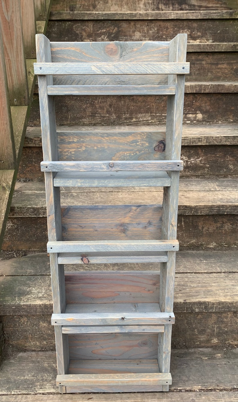 May include: A gray wooden shelf unit with four shelves. The shelves are made of reclaimed wood and have a rustic look. The shelf unit is perfect for displaying small items or organizing a small space.
