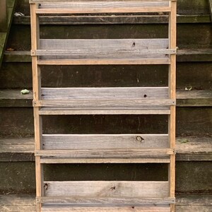 May include: A rustic wooden shelf unit with five shelves. The shelves are made of reclaimed wood and have a natural, weathered finish. The shelf unit is freestanding and has a simple, farmhouse style.