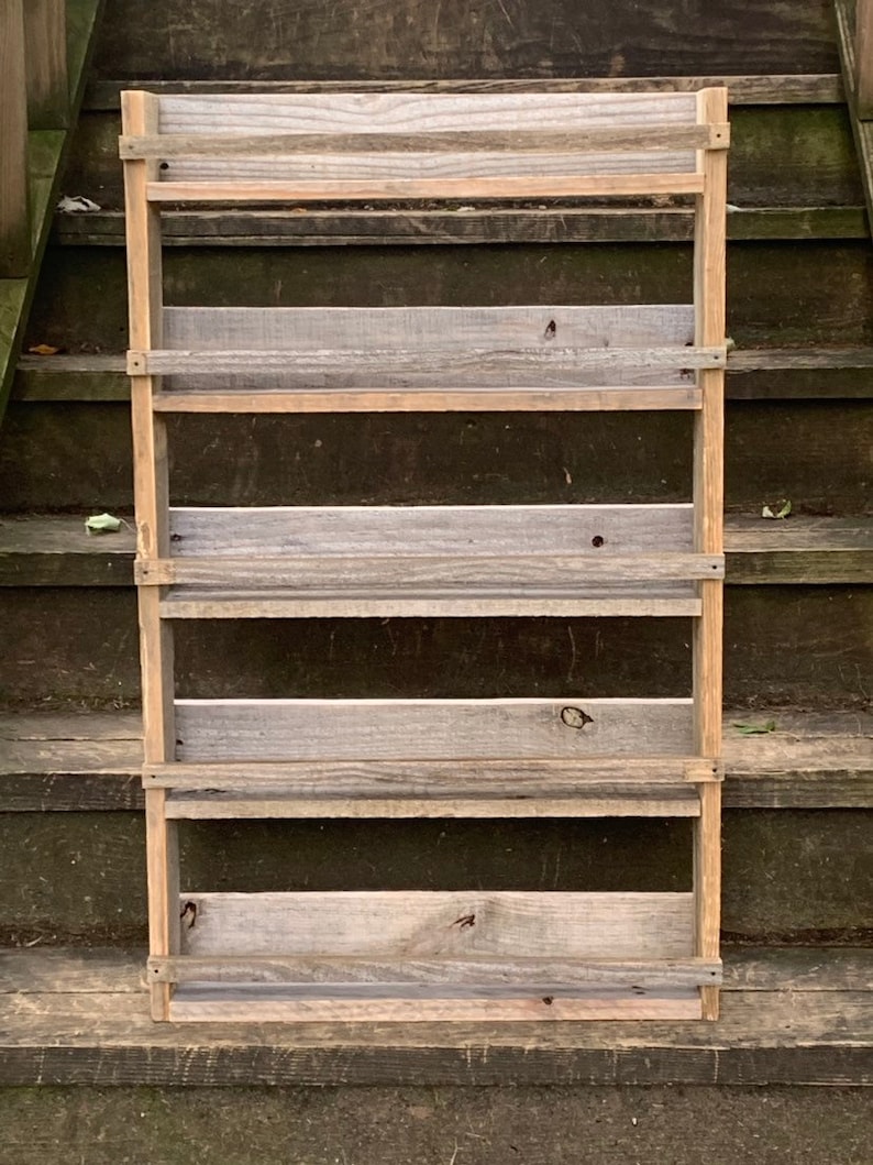 May include: A rustic wooden shelf unit with five shelves. The shelves are made of reclaimed wood and have a natural, weathered finish. The shelf unit is freestanding and has a simple, farmhouse style.