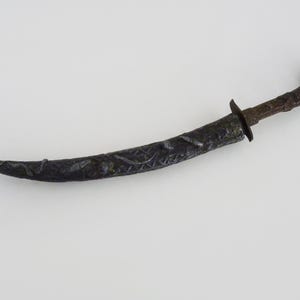 May include: A black metal dagger with an ornate design on the blade and handle.