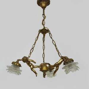Puede incluir: L&aacute;mpara de ara&ntilde;a antigua de lat&oacute;n con tres figuras de querubines que sostienen pantallas de cristal esmerilado. La l&aacute;mpara tiene un soporte de techo decorativo y suspensi&oacute;n de cadena. Una l&aacute;mpara cl&aacute;sica.