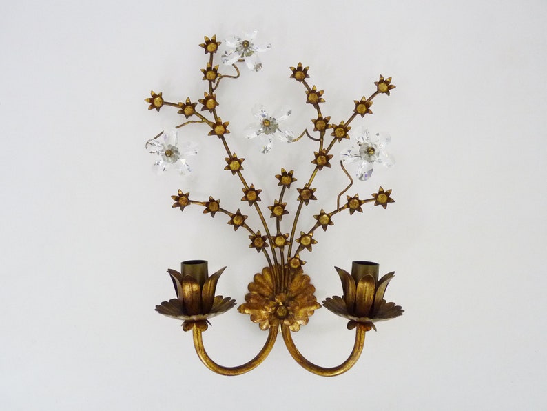 May include: Gold wall sconce with a floral design featuring crystal flowers and two candle holders.