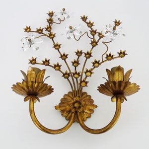 May include: Gold metal wall sconce with two light fixtures and a floral design. The sconce has a gold finish and features crystal accents.