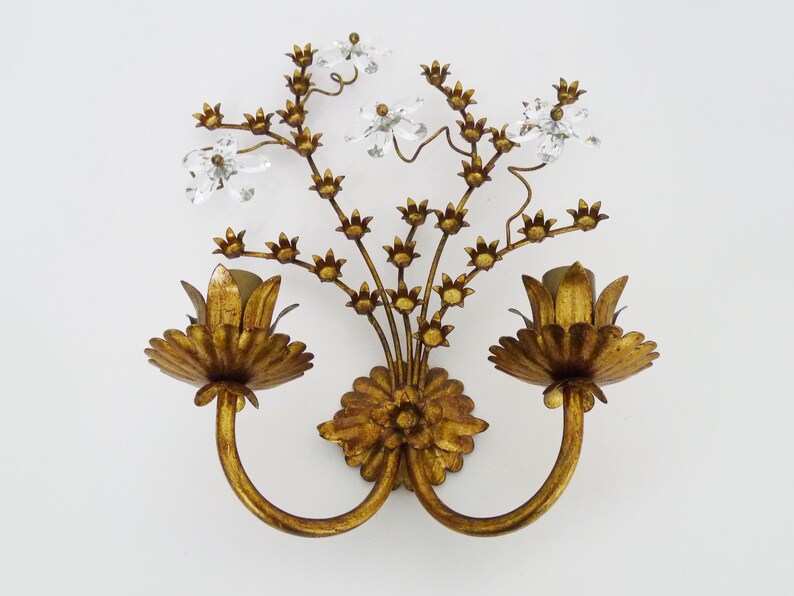 May include: Gold metal wall sconce with two light fixtures and a floral design. The sconce has a gold finish and features crystal accents.