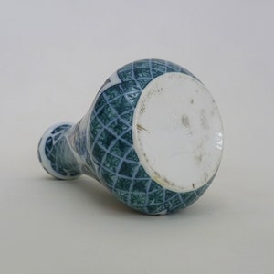 May include: A blue and white ceramic vase with a geometric pattern. The vase has a round base and a narrow neck.