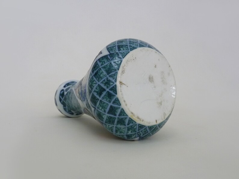 May include: A blue and white ceramic vase with a geometric pattern. The vase has a round base and a narrow neck.