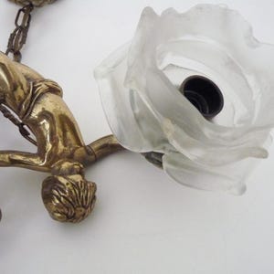 Puede incluir: Aplique de pared de lat&oacute;n antiguo con una figura estilizada y una pantalla en forma de rosa de cristal esmerilado. La l&aacute;mpara incluye una cadena y elementos decorativos.
