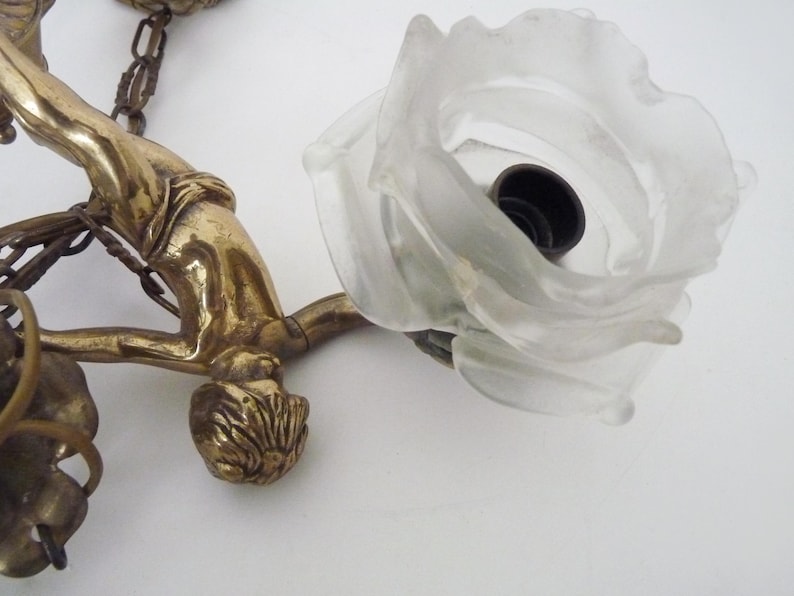 Puede incluir: Aplique de pared de lat&oacute;n antiguo con una figura estilizada y una pantalla en forma de rosa de cristal esmerilado. La l&aacute;mpara incluye una cadena y elementos decorativos.