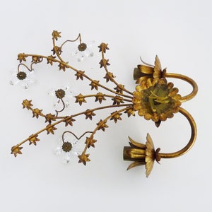 May include: Gold metal wall sconce with a floral design and clear crystal accents. The sconce has two arms that curve upwards and are decorated with leaves and flowers. The sconce is perfect for adding a touch of elegance to any room.