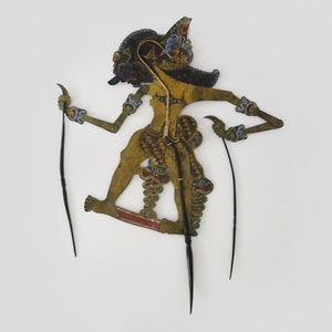 Puede incluir: Un títere de sombras javanés tradicional, o wayang kulit, que representa a un personaje con un traje colorido y detallado y una corona. El títere está hecho de cuero y pintado con detalles dorados, rojos, azules y verdes. Se sostiene con dos varillas.