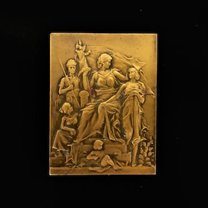 Peut inclure: Une sculpture en bronze en relief représentant un groupe de cinq personnages. La figure centrale est une femme assise sur un trône, tenant un drapeau. Les autres personnages sont debout autour d'elle, certains tenant des objets. La sculpture est placée sur un fond de feuillage.