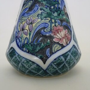 May include: A small, ceramic vase with a conical shape. The vase is decorated with a blue, green, and yellow floral pattern. The base of the vase has a green and white geometric pattern.