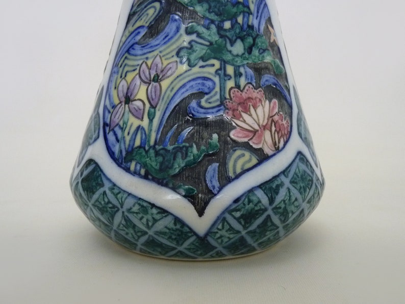 May include: A small, ceramic vase with a conical shape. The vase is decorated with a blue, green, and yellow floral pattern. The base of the vase has a green and white geometric pattern.