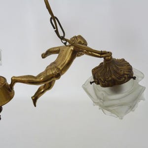 Puede incluir: Candelabro antiguo de lat&oacute;n con una figura de querub&iacute;n que sostiene una l&aacute;mpara. La l&aacute;mpara tiene un dise&ntilde;o decorativo y ornamentado con pantallas de vidrio esmerilado. El dise&ntilde;o general es vintage y elegante.