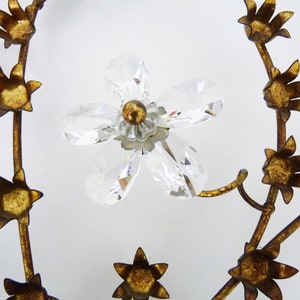 May include: A gold metal floral wreath with crystal accents. The wreath is made of metal branches with small gold flowers and a larger crystal flower in the center.