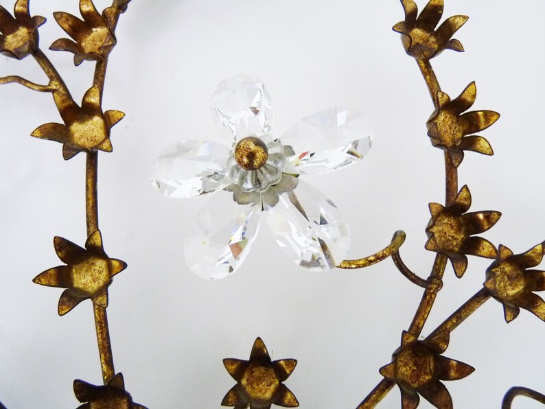 May include: A gold metal floral wreath with crystal accents. The wreath is made of metal branches with small gold flowers and a larger crystal flower in the center.