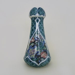 May include: A ceramic bottle stopper with a green, blue, and white floral design. The stopper is shaped like a teardrop with a rounded top.