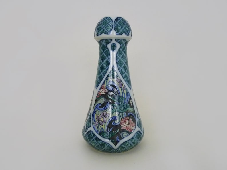 May include: A ceramic bottle stopper with a green, blue, and white floral design. The stopper is shaped like a teardrop with a rounded top.