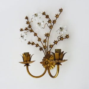 May include: Gold metal wall sconce with a floral design featuring crystal accents. The sconce has two light bulbs and a curved arm.