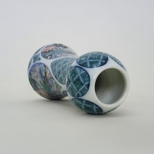 May include: A white ceramic vase with a blue and green geometric pattern and a floral design. The vase has a wide mouth and a narrow base.