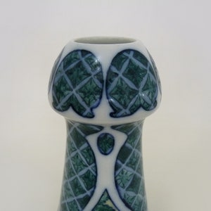 May include: A white ceramic vase with a green and blue geometric pattern. The vase has a wide mouth and a narrow base.