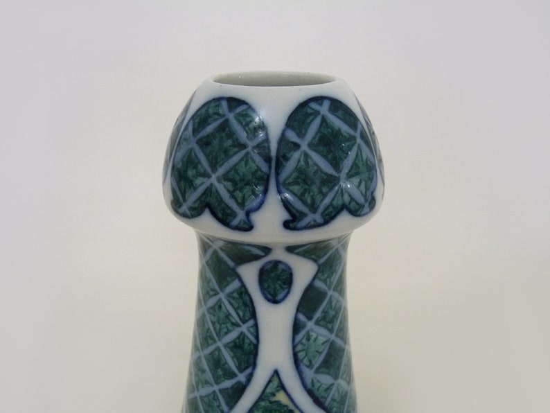 May include: A white ceramic vase with a green and blue geometric pattern. The vase has a wide mouth and a narrow base.