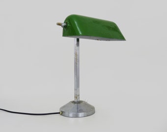 Könnte beinhalten: Eine grüne Metall-Tischlampe mit einem silbernen Sockel und einem langen, verstellbaren Arm. Die Lampe hat ein schlichtes Design und ist in gutem Zustand.
