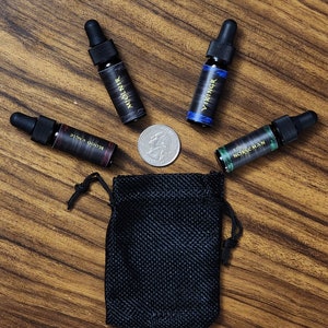 May include: Four small glass bottles with black labels and gold lettering. The bottles contain essential oils or perfumes. The labels read "Blood Eagle", "The Norsemen", "Mjolnir", and "Vikingr". A black drawstring bag is in the center of the image.