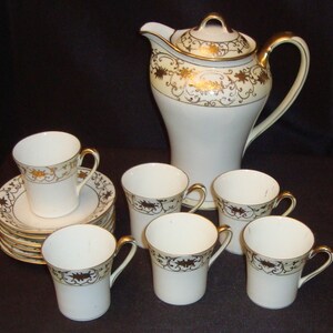 Puede incluir: Un juego de té de porcelana blanca con detalles dorados. El juego incluye una tetera, seis tazas y seis platillos. Las tazas y los platillos tienen un delicado diseño floral.