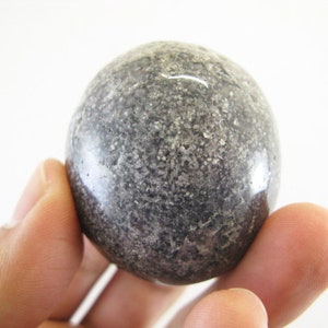 May include: A smooth, round, gray and black stone sphere. The sphere has a speckled, textured surface.