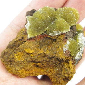 May include: A cluster of yellow-green crystals on a brown, rocky matrix. The crystals are clustered together in a rounded shape, and they have a rough, textured surface.