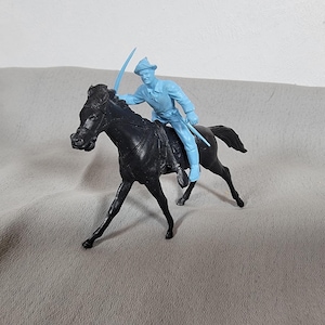 May include: A vintage toy soldier on horseback. The horse is black, and the rider is light blue, holding a sword. The toy is made of plastic and is a classic representation of a historical figure. The toy is a collectible item.
