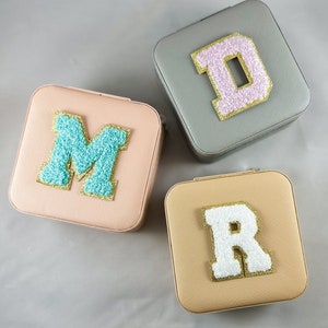 May include: Three square jewelry boxes with different colored lids. Each lid has a large, fluffy letter on it. The letters are D, M, and R. The letters are outlined in gold.
