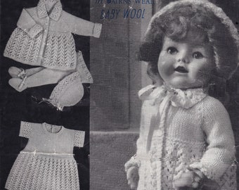 May include: A knitted doll outfit in white with a crocheted jacket, dress, trousers, and hat. The outfit is made with "Baby Wool" yarn and is part of the "In Bairns Wear" line.